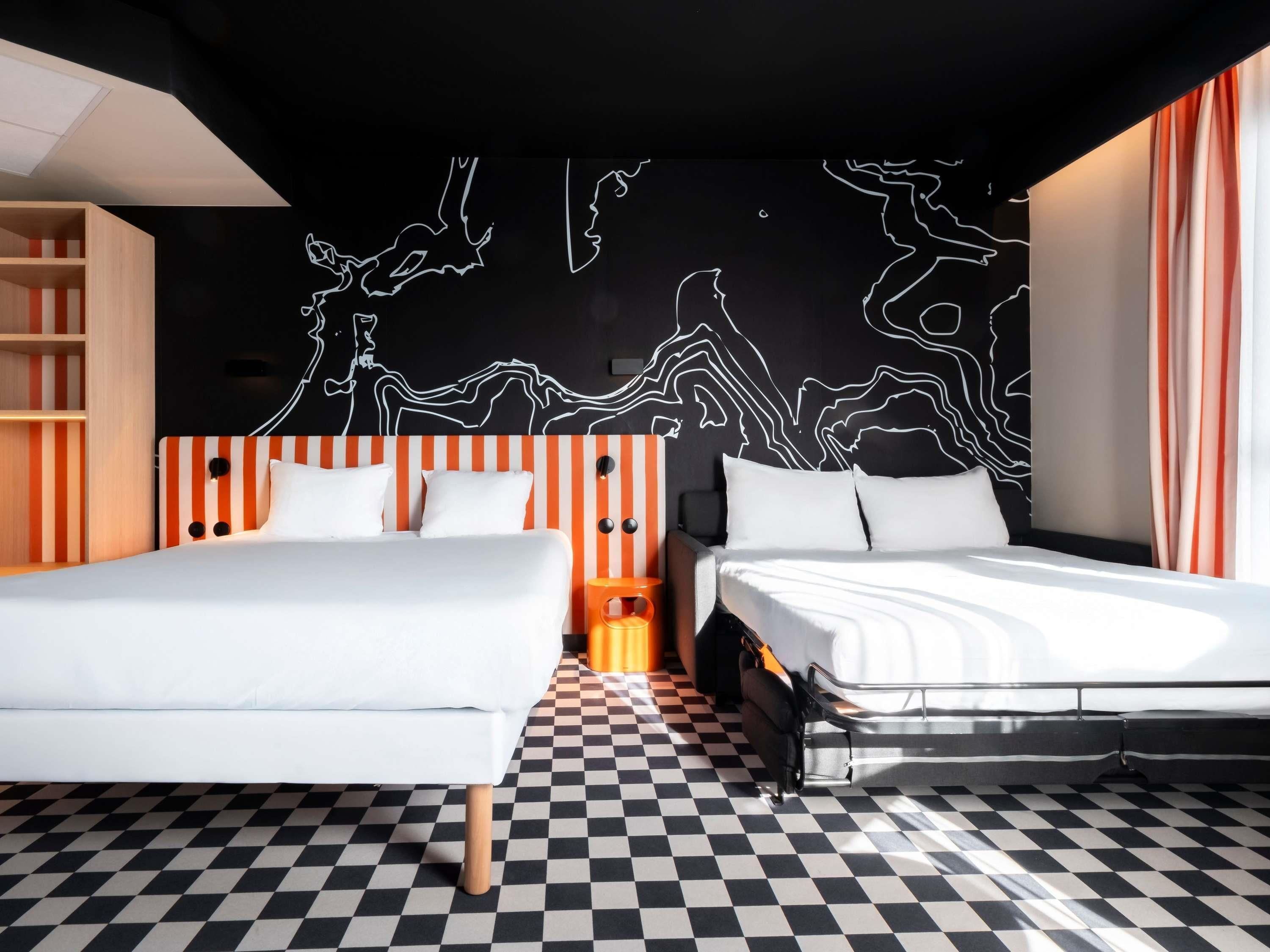 A modern hotel room with a checkered floor, two beds with white bedding, a black and white abstract wall art, and a striped orange headboard.