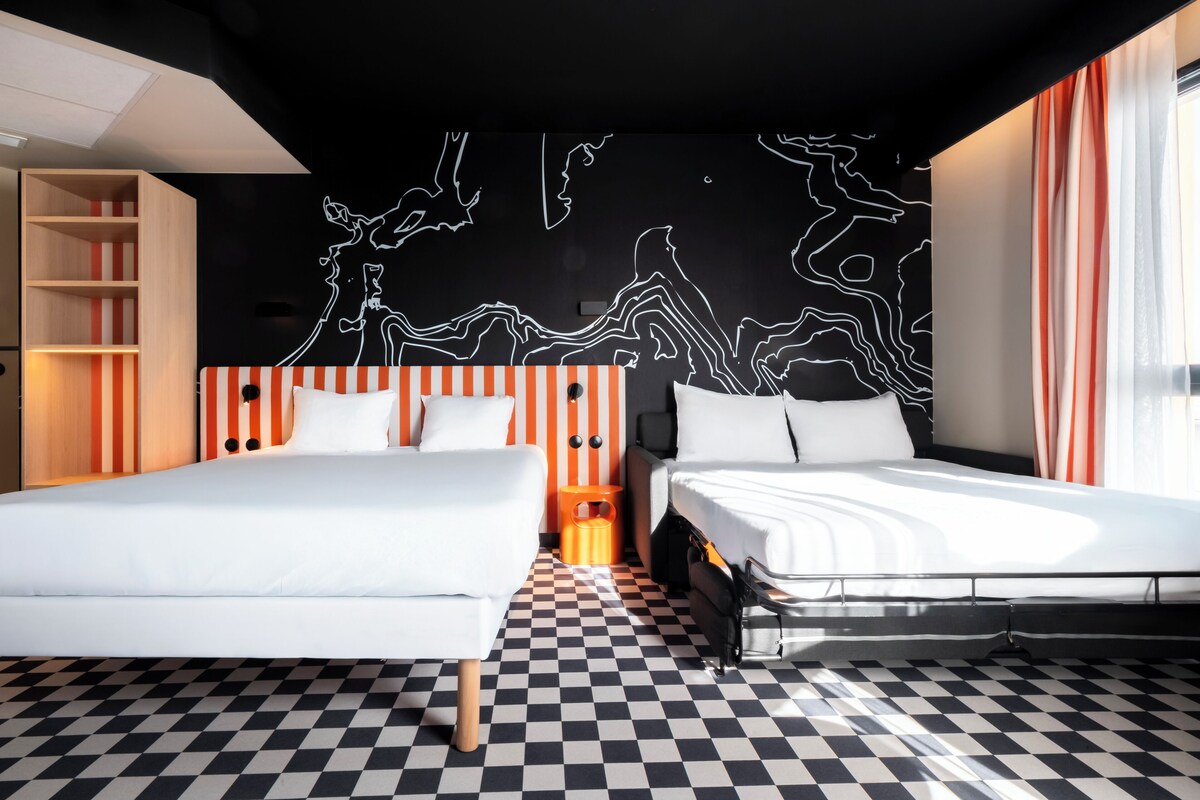 Une chambre d’hôtel moderne avec deux lits, un sol à carreaux, une œuvre d’art abstraite en noir et blanc au mur et une bibliothèque en bois.