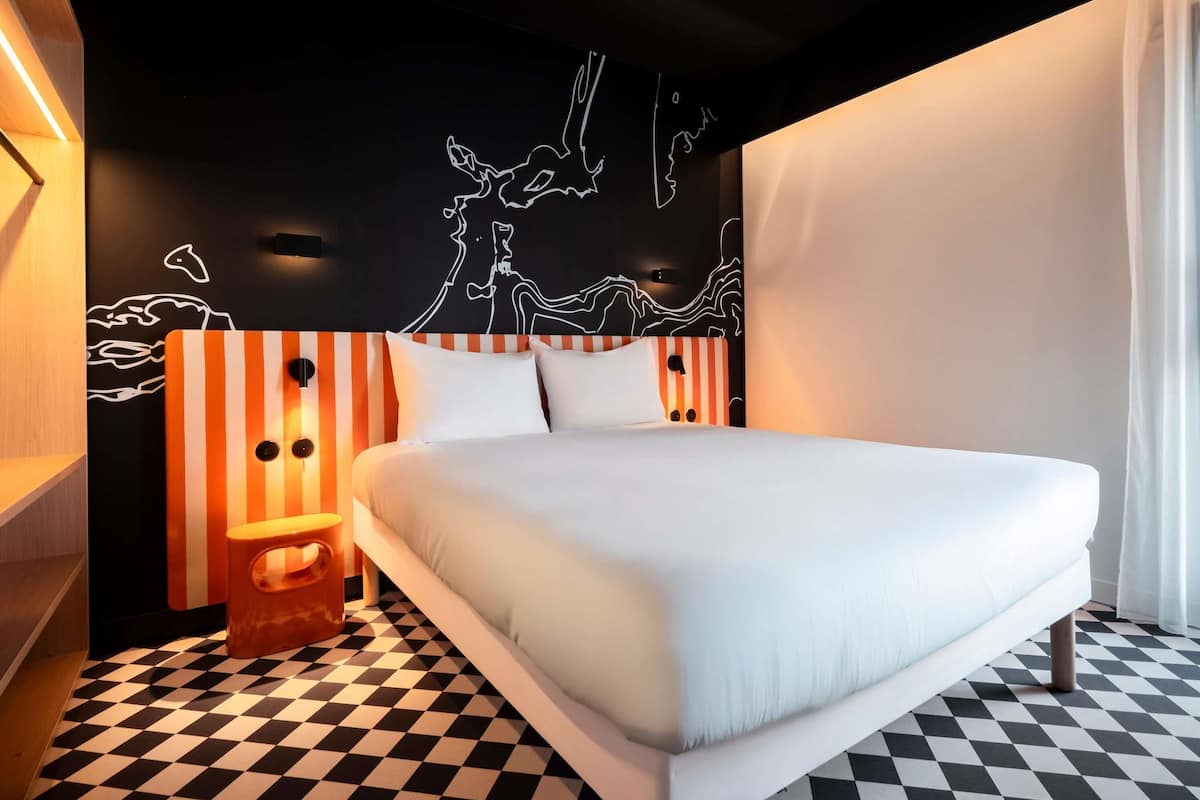 A modern hotel room with a large bed, striped headboard, and a black and white checkered floor.