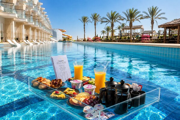 A poolside breakfast setup with a variety of foods and drinks, including waffles, fruits, and a juice box.