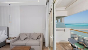 Una camera moderna con divano, letto, tavolino in legno e un balcone vista mare.