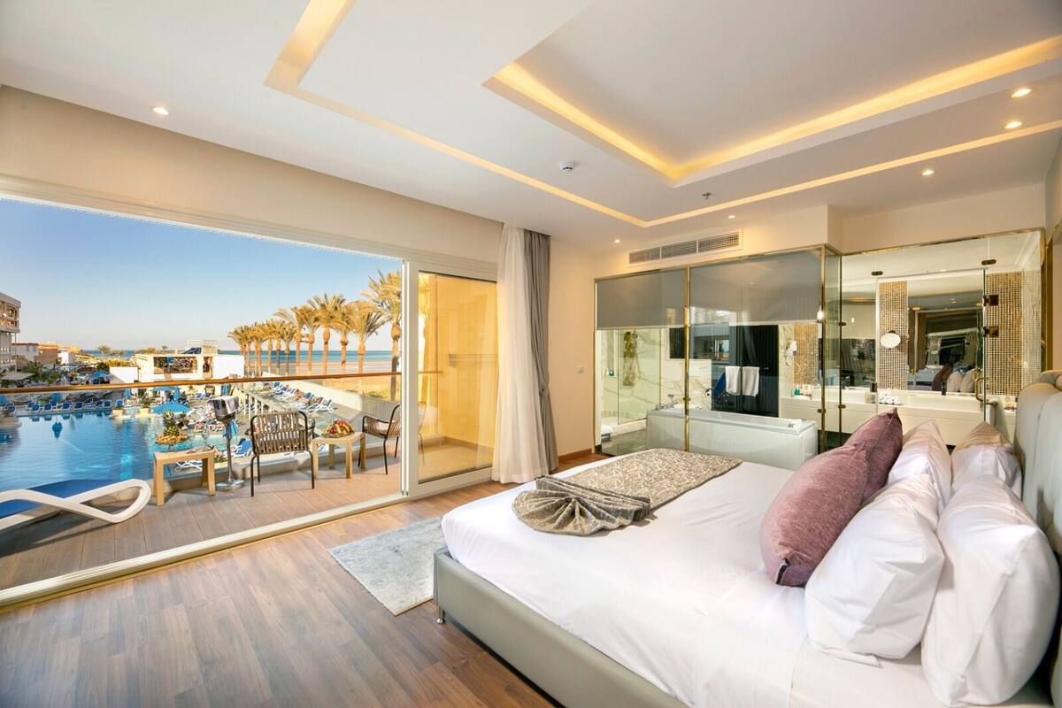 A hotel room with a bed, a view of a pool, and a balcony.