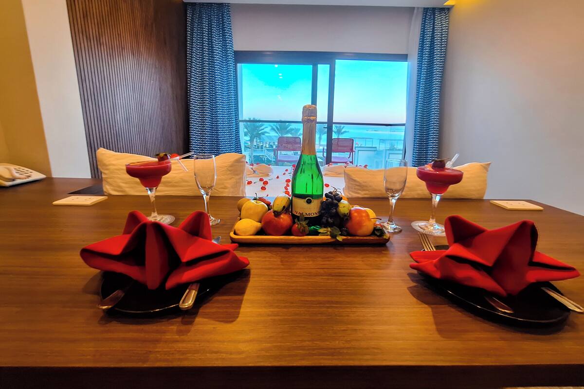 A dining table with a bottle of champagne, fruit, and red napkins.