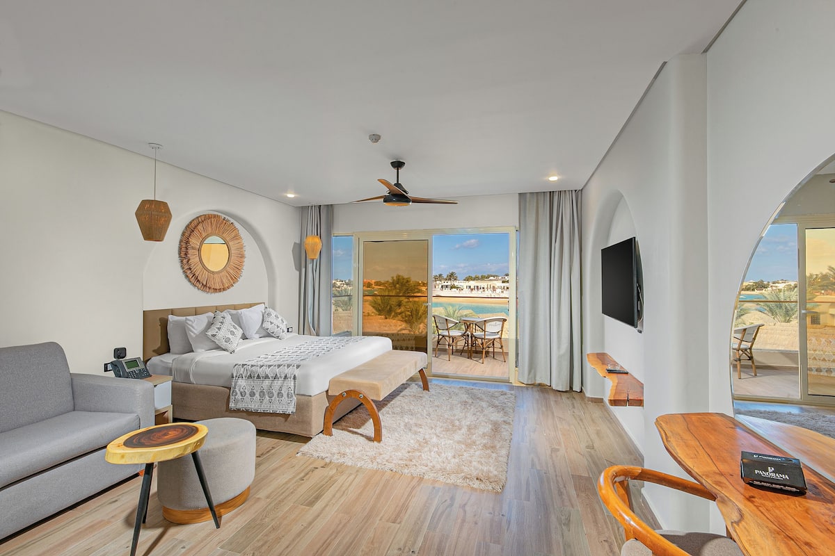 Een moderne slaapkamer met een bed, bank, houten bijzettafeltje en uitzicht op het groen.