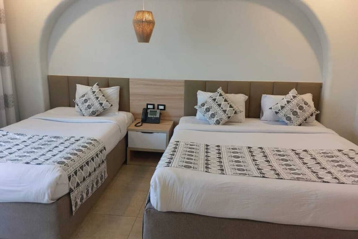 Een hotelkamer met twee bedden, elk voorzien van beddengoed met een patroon, een nachtkastje met een telefoon en een hanglamp.