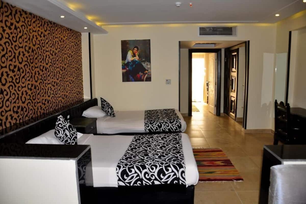Hotelkamer met twee bedden, een behang met patroon, een schilderij en uitzicht op de gang.