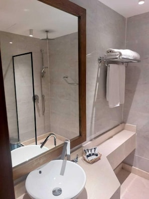 Une salle de bain moderne avec un grand miroir, un lavabo, une douche et un porte-serviettes.