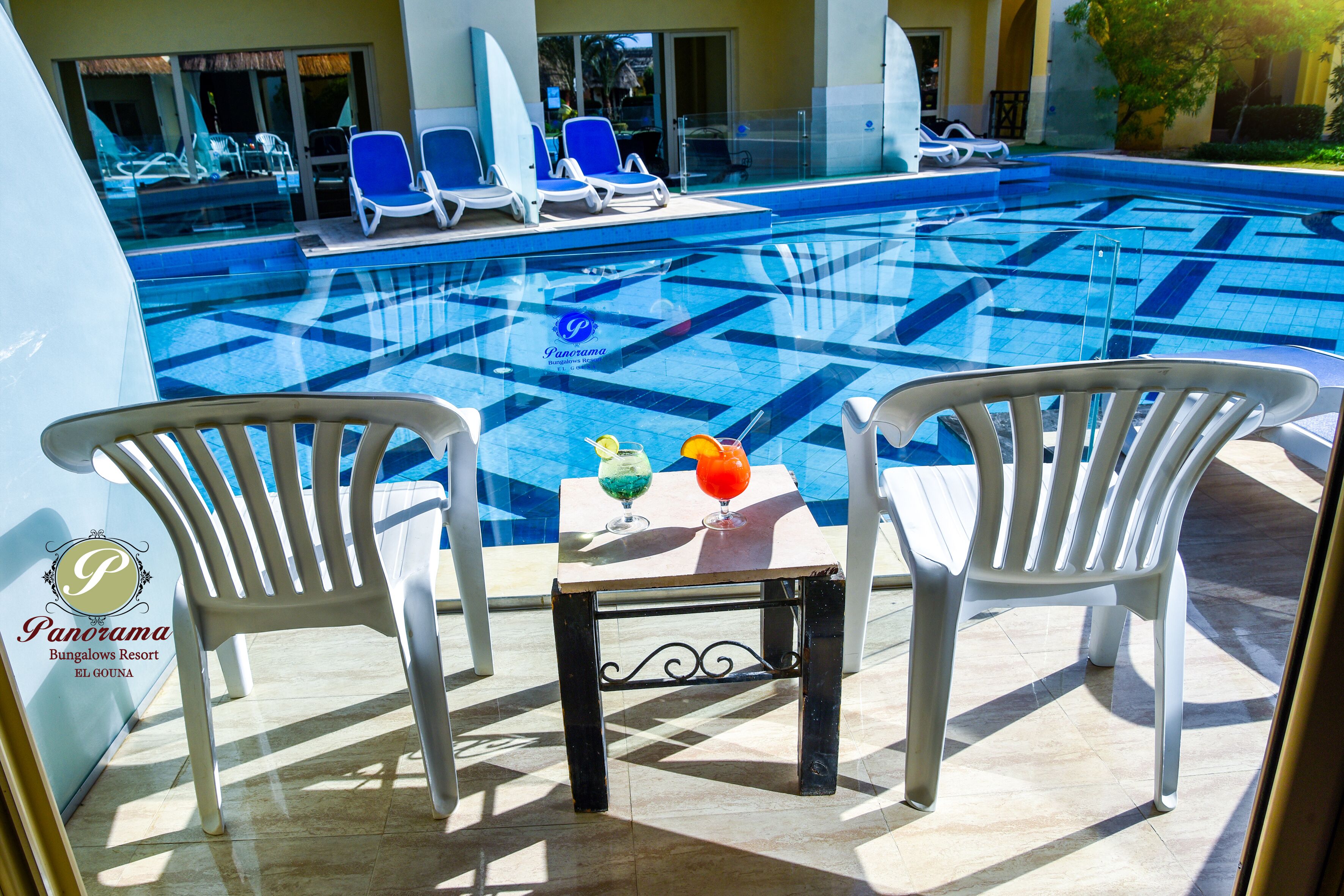 Área da piscina com espreguiçadeiras e uma mesa com bebidas.