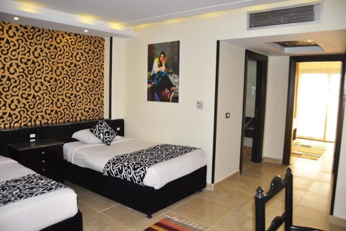 Een hotelkamer met twee bedden, een decoratief paneel, een schilderij en uitzicht op de gang.