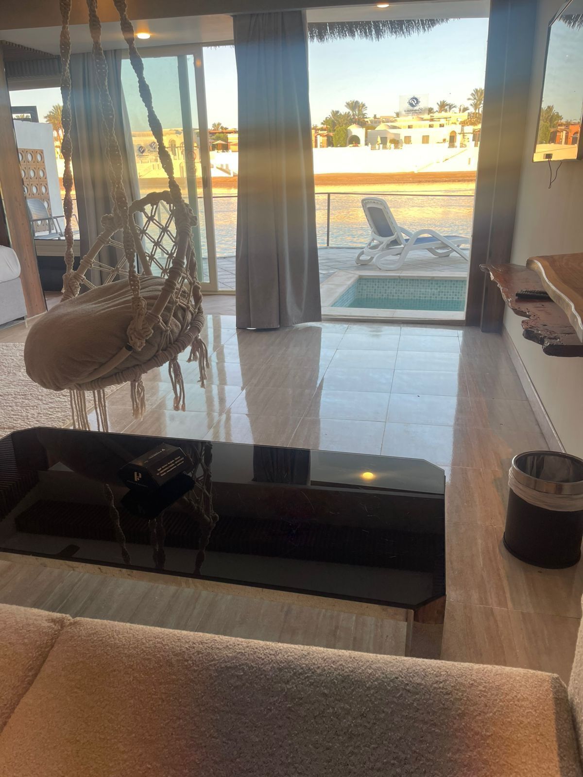 Una habitación amplia con un gran ventanal, una silla colgante, una piscina pequeña y vistas del entorno.