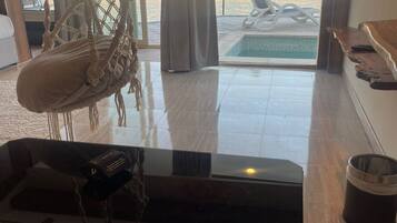 Una habitación amplia con un gran ventanal, una silla colgante, una piscina pequeña y vistas del entorno.