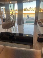 Una habitación amplia con un gran ventanal, una silla colgante, una piscina pequeña y vistas del entorno.