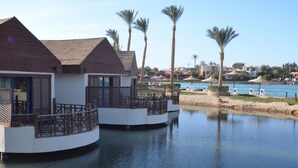 A waterfront hotel with overwater bungalows, palm trees, and a pool area.