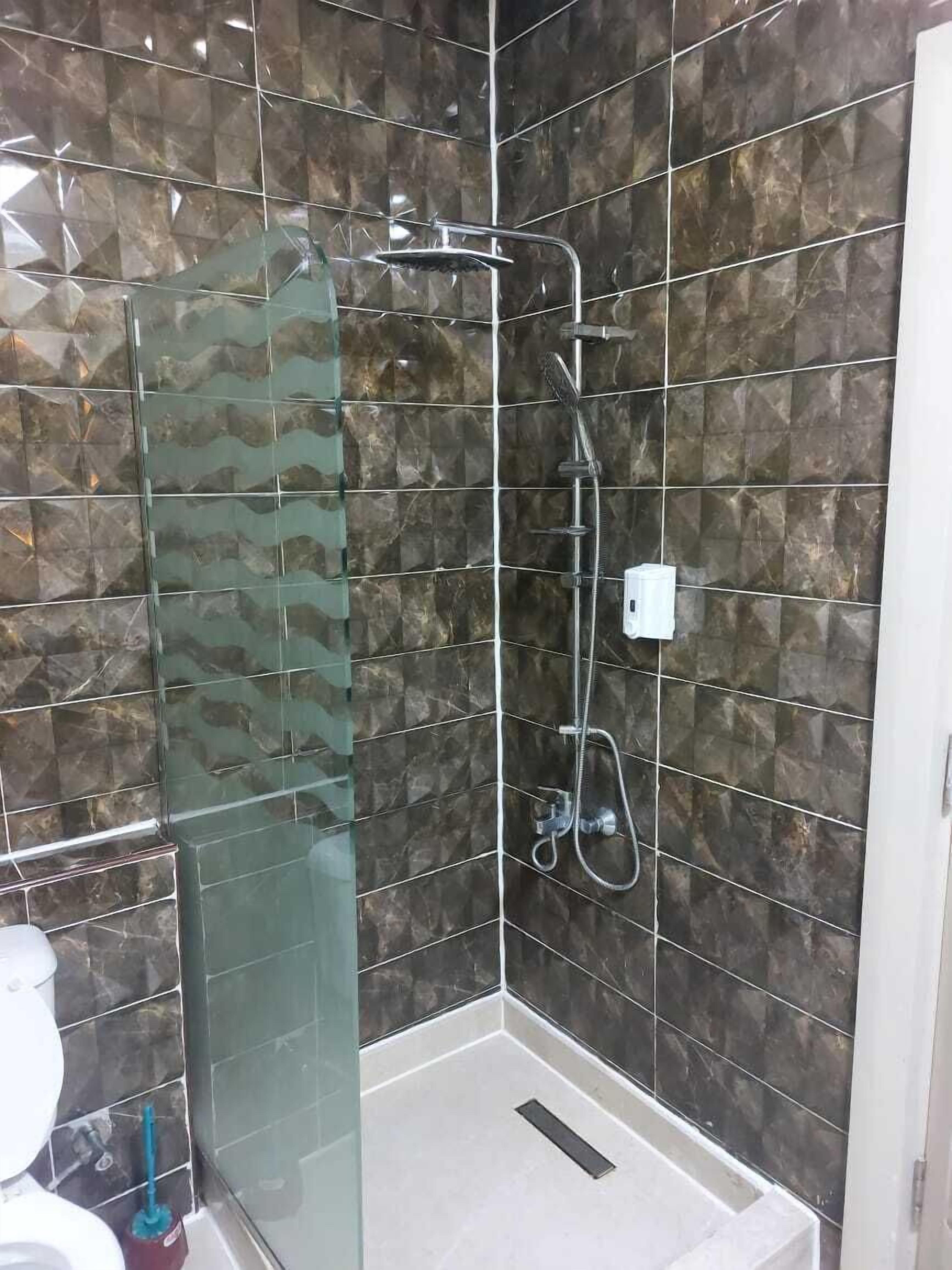 Un baño con cabina de ducha de vidrio, cabezal de ducha manual y un accesorio de ducha de mano.