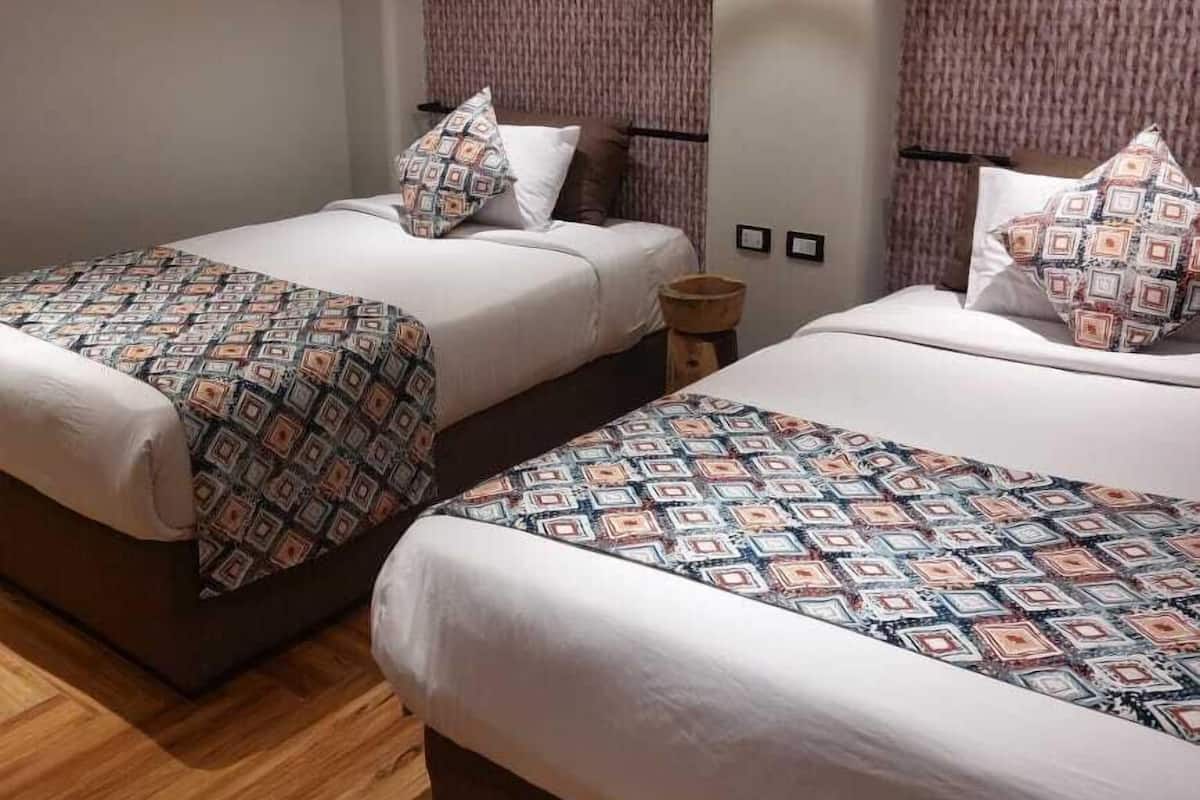 Een hotelkamer met twee bedden, beddengoed met een patroon, een hanglamp en een gestructureerde wand.