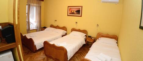 A hotel room with two wooden beds, a small desk with a television, a heater, and a picture on the wall.