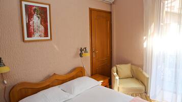 A hotel room with a bed, a chair, a door, and a painting on the wall.