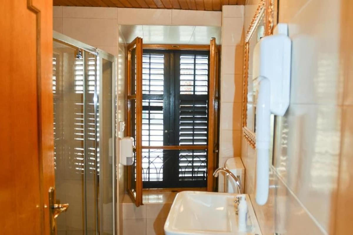 A bathroom with a wooden ceiling, a glass shower enclosure, a sink with a white faucet, and a patterned floor.