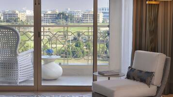 A room with a view of a cityscape, a white wicker chair, a white sofa with a striped pillow, and a tall floor lamp.