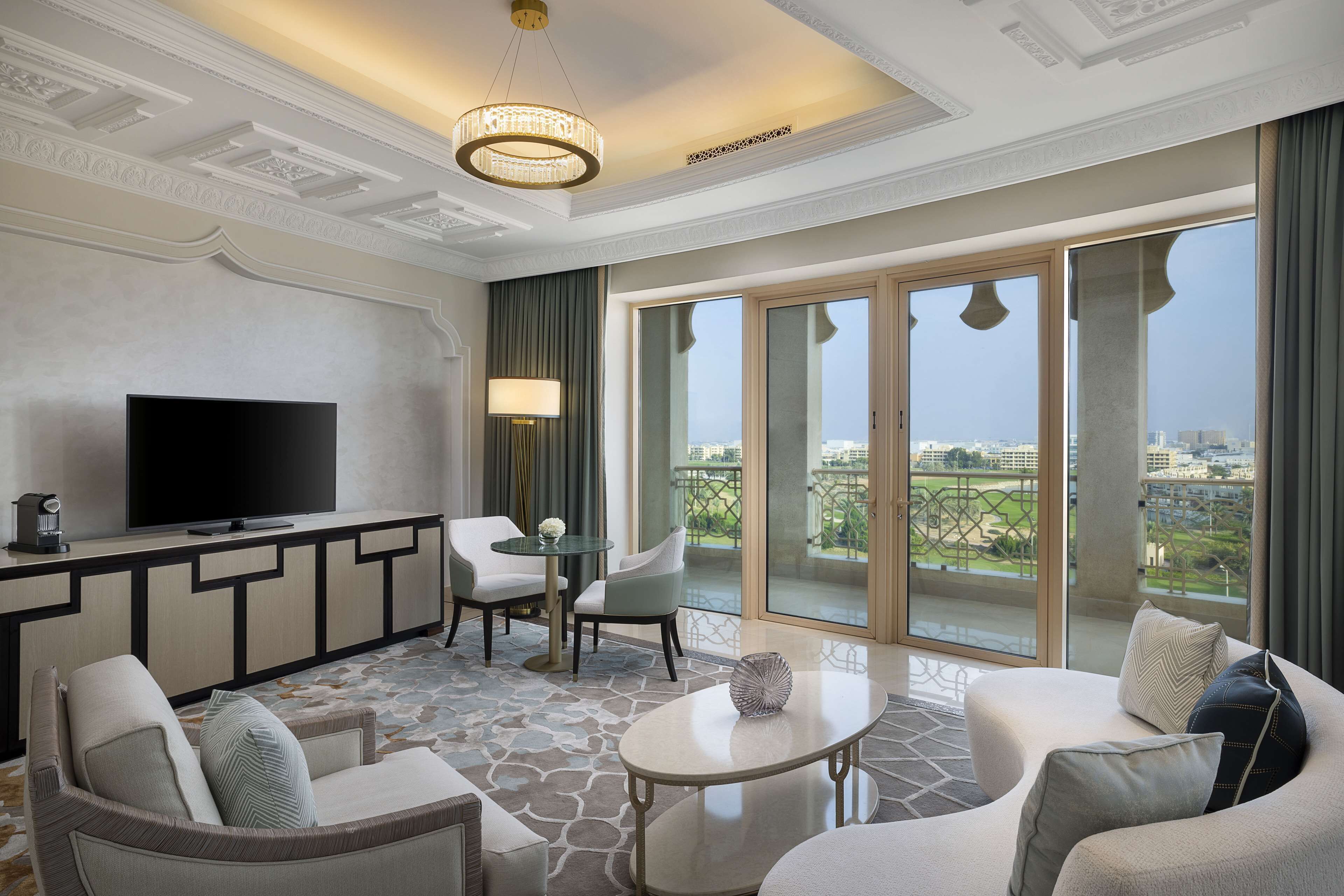 A modern hotel room with a flat-screen TV, comfortable seating, a dining area, and a balcony with a city view.