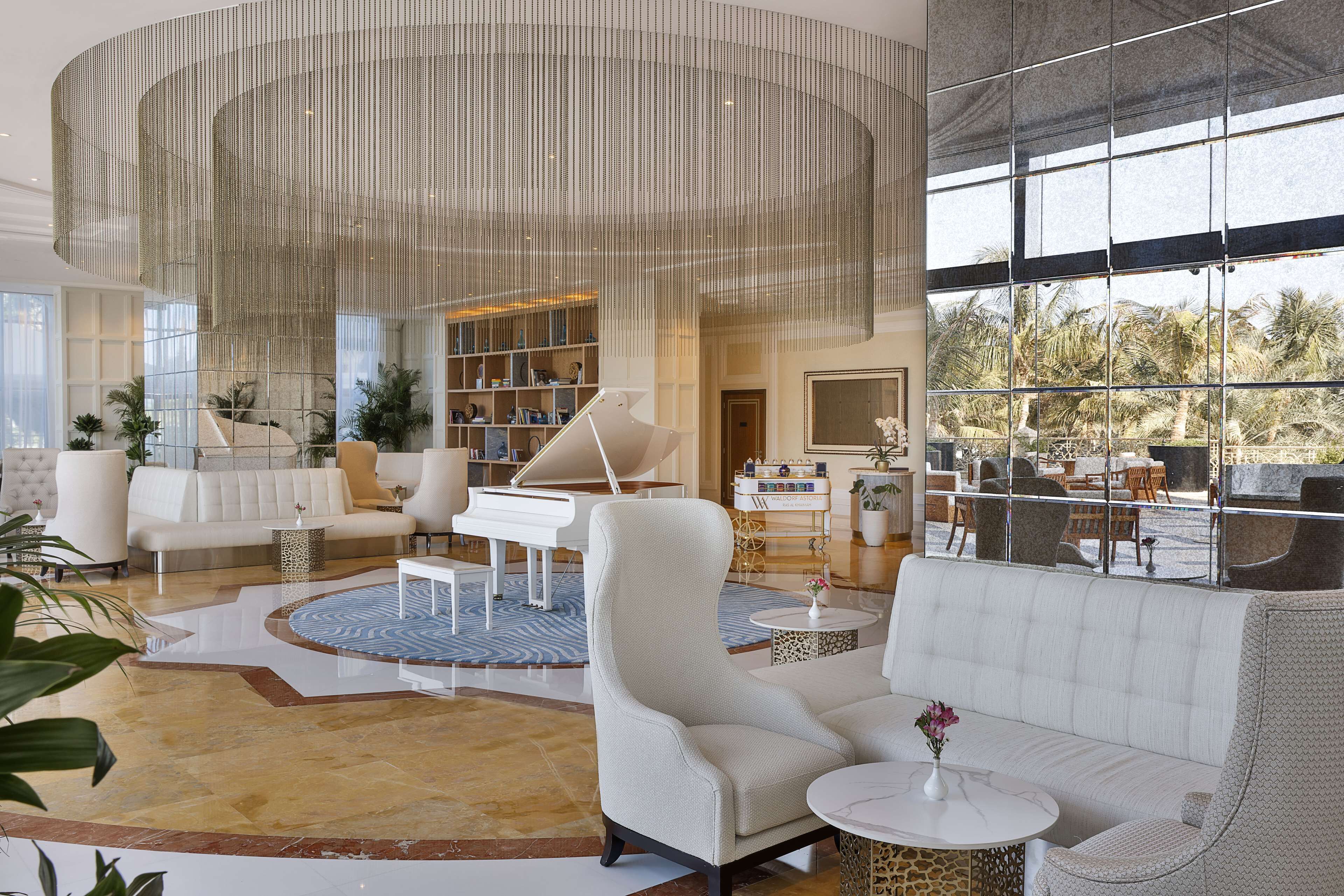 Eine geräumige Lobby mit einem Flügel, komfortablen Sitzgelegenheiten und einem großen Fenster mit Blick auf Palmen.