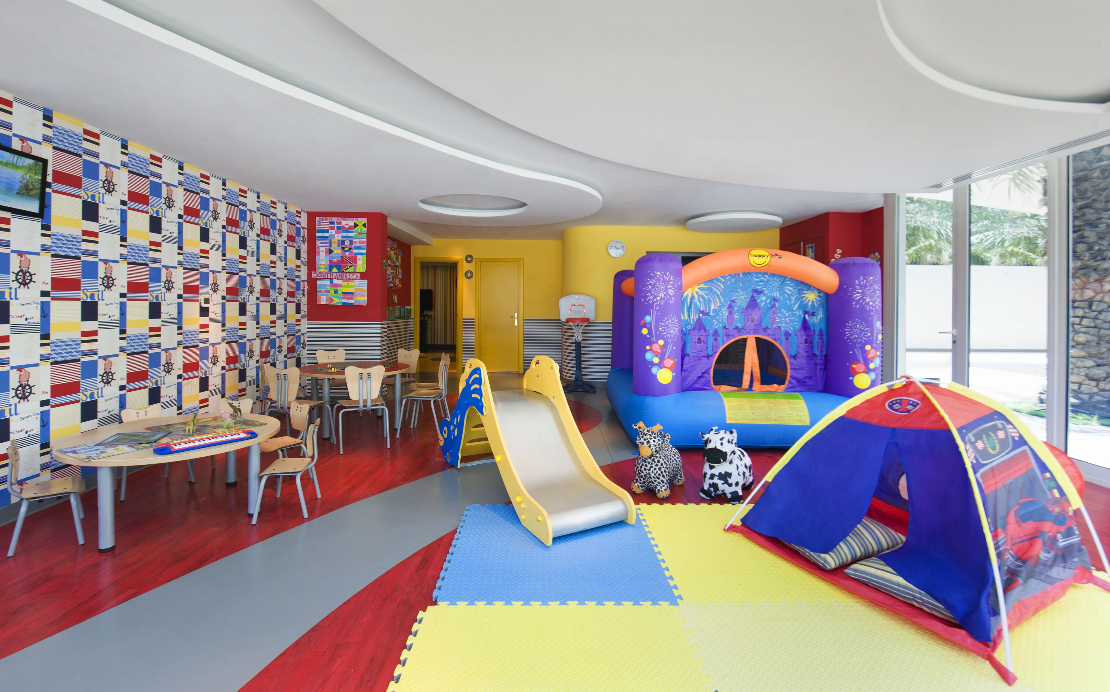A children's play area with a slide, inflatable play structures, and a wall decorated with maritime-themed tiles.