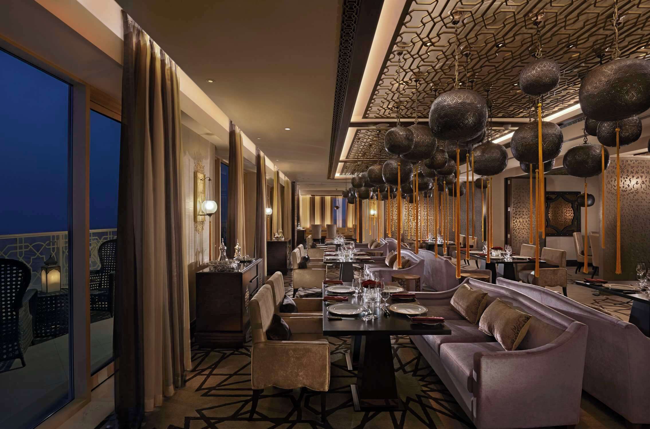 A well-lit, elegantly furnished dining area with high ceilings and hanging spherical decorations.