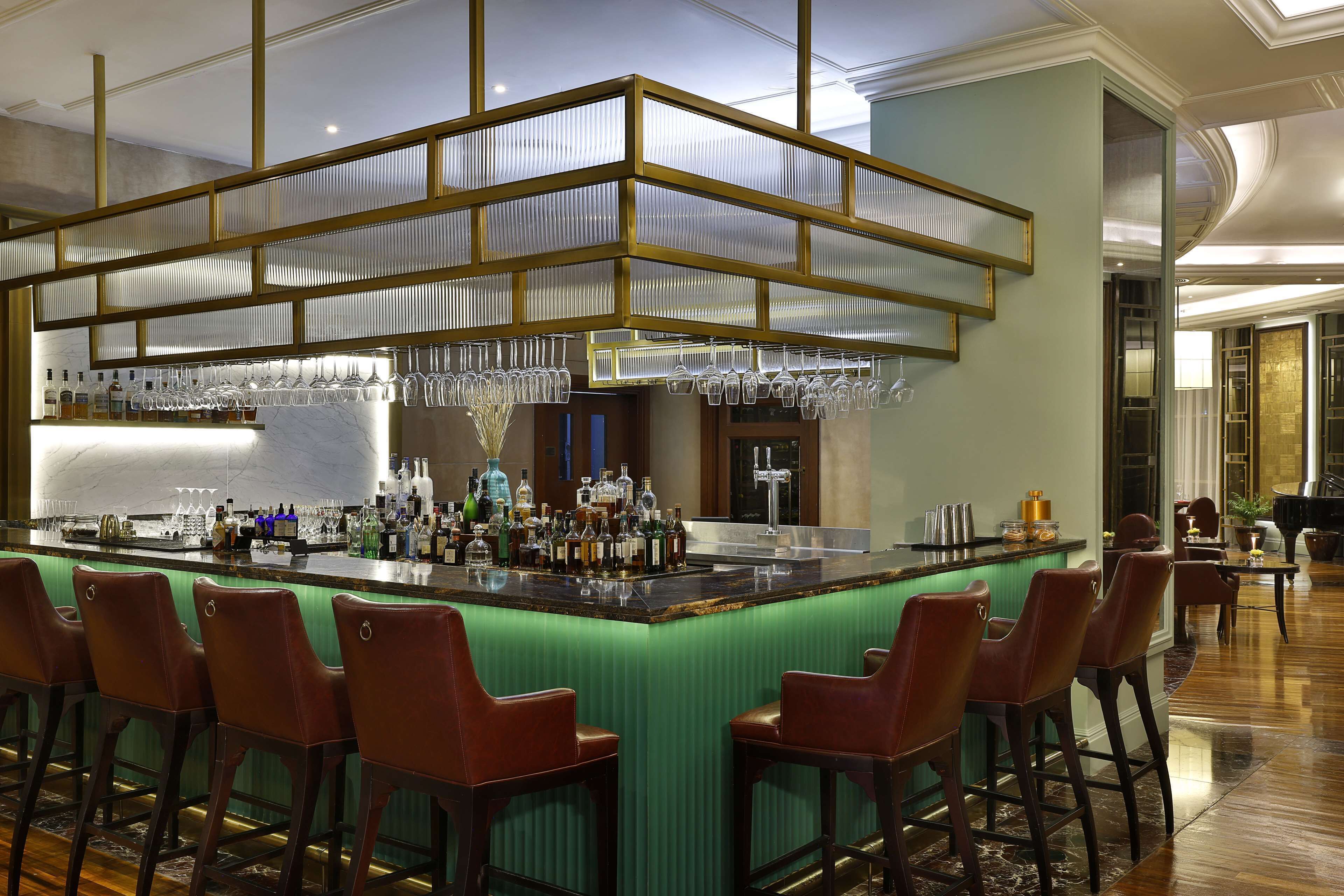 A bar area with a green bar counter, multiple bar stools, and a variety of bottles and glasses.