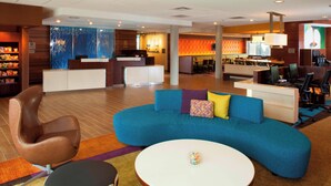 A hotel lobby with a blue sofa, a brown chair, a white table, and a reception desk.
