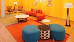 A modern lobby with a curved orange sofa, two blue ottomans, a round coffee table, and two floor lamps.