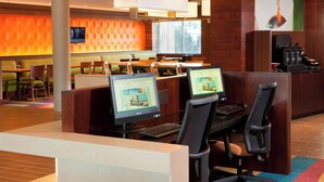 A hotel lobby with computer workstations, a reception desk, and a seating area with a TV screen.