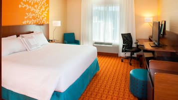 Habitación de hotel con una cama grande, un escritorio con computadora, una silla y un pequeño otoman.