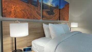 Hotelkamer met een bed, witte beddengoed, nachtkastje met digitale klok, lamp en twee wandlampen.