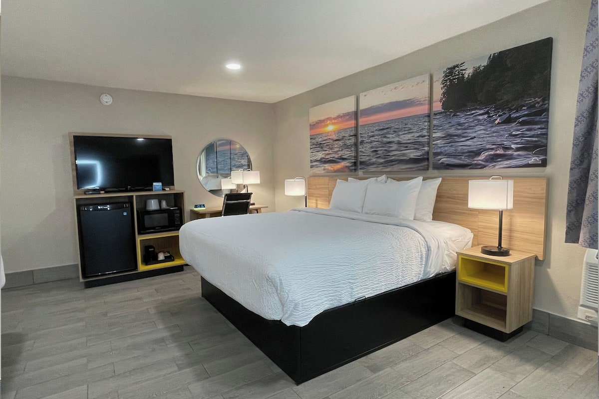 A modern hotel room with a large bed, a flat-screen TV, a mini-fridge, a microwave, and a coffee machine.