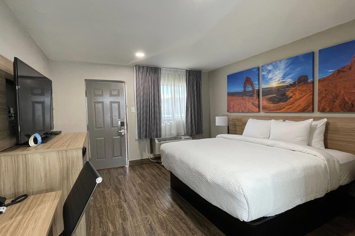Una habitación de hotel con una cama, televisión, escritorio y ventana con cortinas.