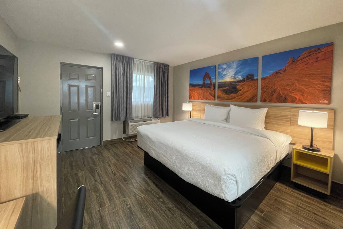 A hotel room with a bed, bedside tables, a desk, and a television.