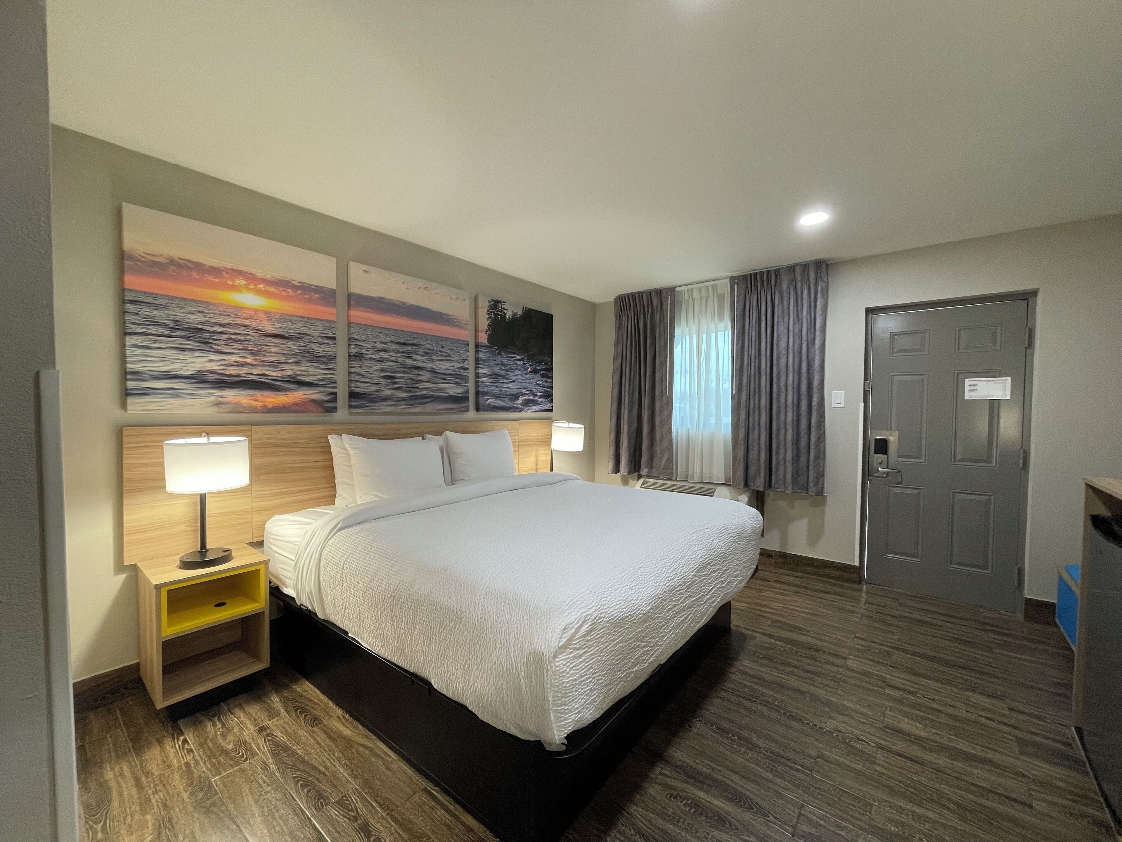 A hotel room with a large bed, two bedside tables with lamps, a door with a lock, and a window with curtains.