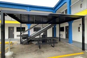 Un espacio al aire libre cubierto con una escalera que lleva a un nivel superior, una mesa y un bote de basura.