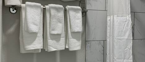 Un baño con inodoro, toallero con toallas dobladas, cortina de ducha y dispensador de papel higiénico.