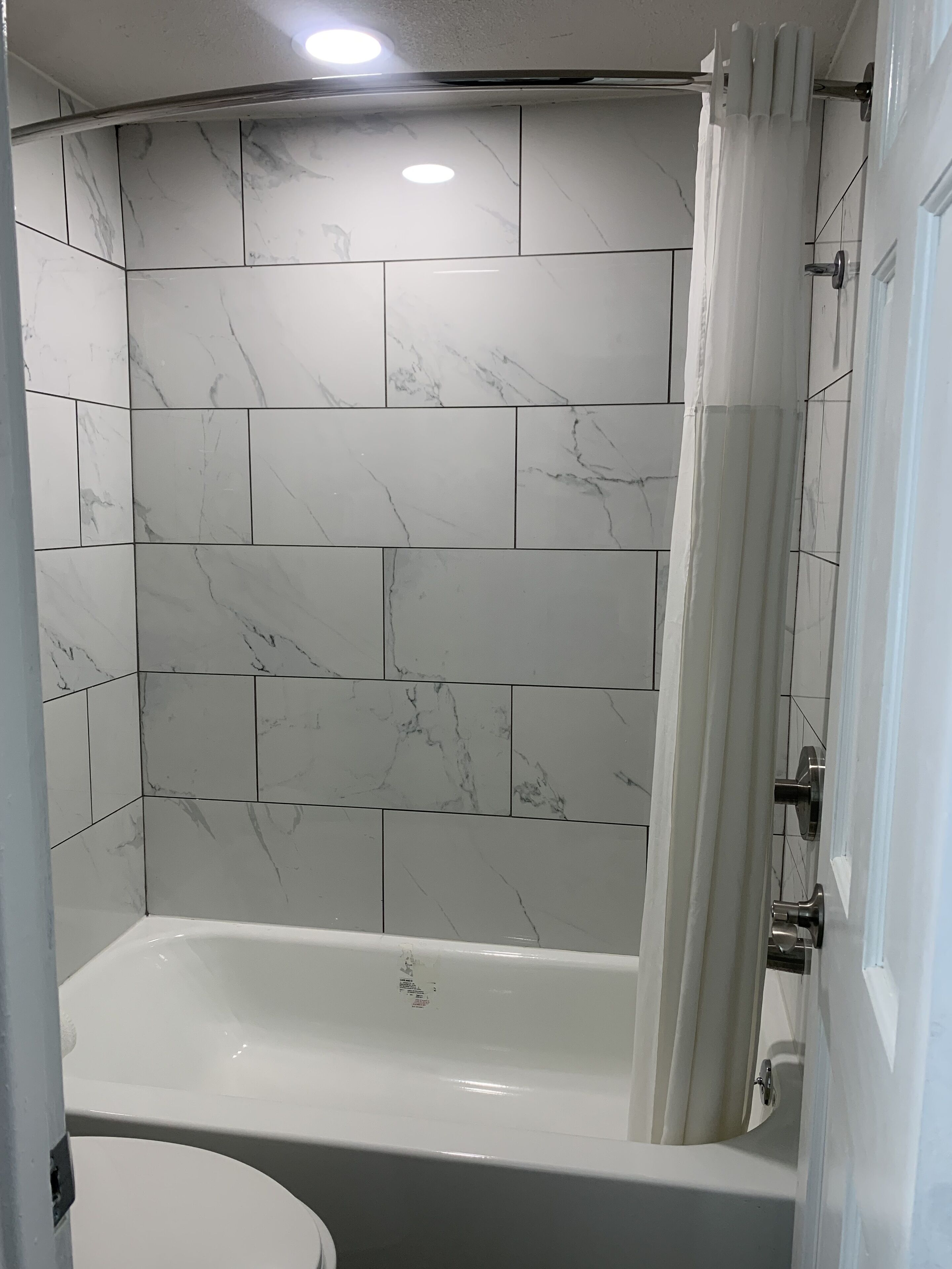 A bathroom with white marble tiles, a bathtub, and a shower curtain.