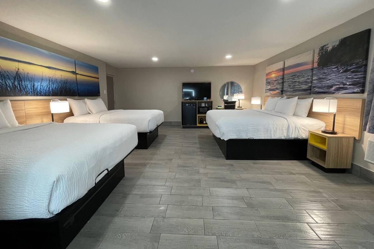 A hotel room with two beds, a TV, a desk, and artwork on the walls.