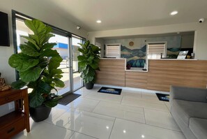 A reception area with a reception desk, two large potted plants, a sofa, and a wall-mounted artwork. - Days Inn by Wyndham Sulphur Springs (Sulphur Springs)