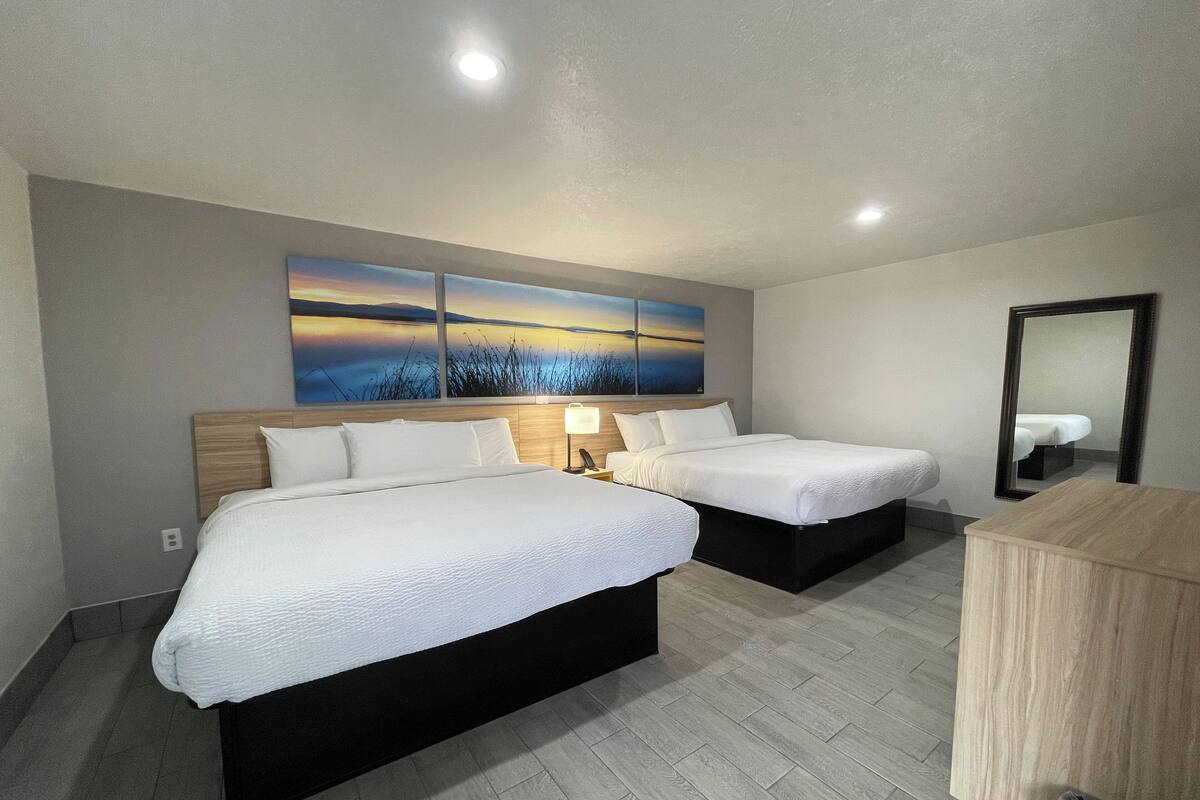 A hotel room with two beds, a large painting above the beds, a wooden headboard, a nightstand with a lamp, and a mirror on the wall.