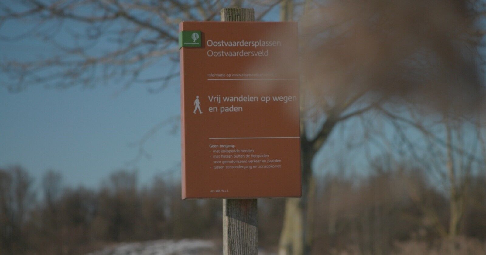 A sign with text in Dutch, likely providing information about a park or outdoor area.