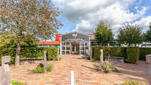 Een hotelentree met een met baksteen bestraat pad dat naar een gebouw leidt, waarop 'Hotel - Restaurant - Toilet' staat.