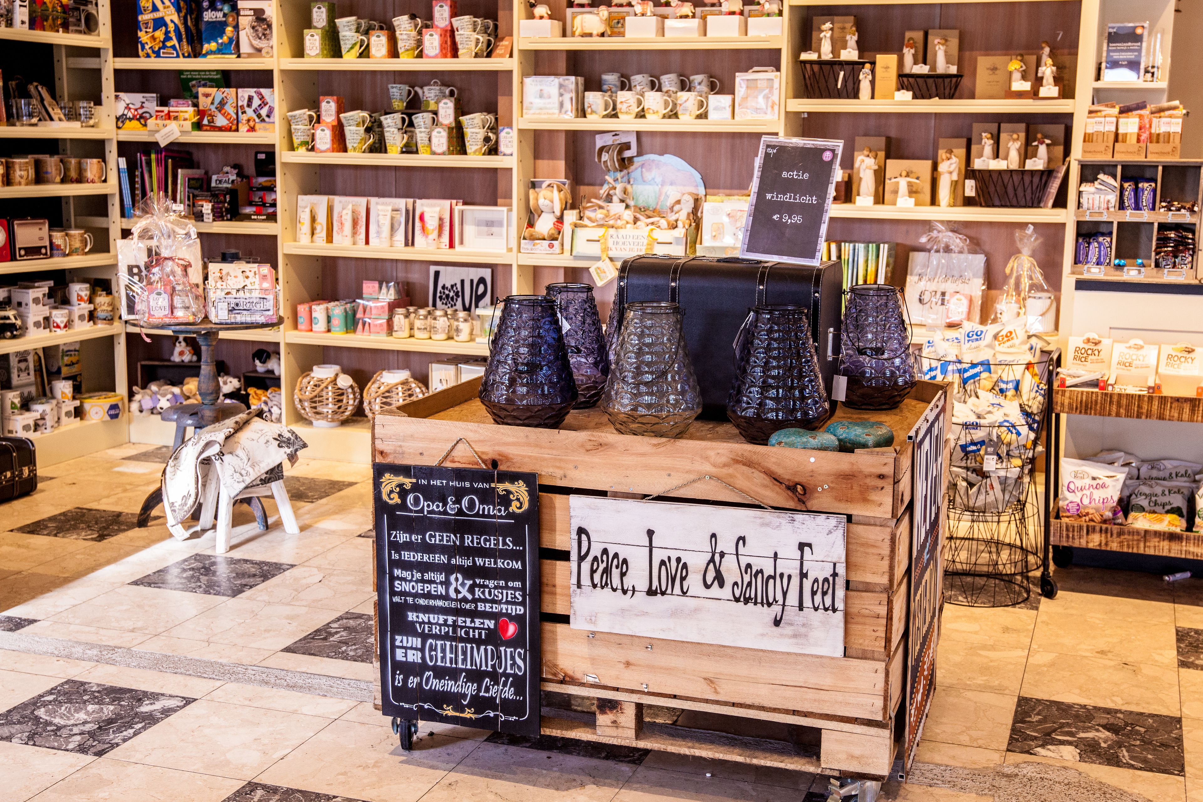 A store with shelves of various items, including mugs and ceramics. There are signs with text and a display of glass bottles.
