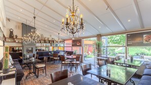 Een ruim restaurant met hoge plafonds, kroonluchters en diverse zitplaatsen, waaronder tafels en een bank.