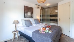 Een moderne slaapkamer met een groot bed, een nachtkastje met een lamp, een wandairconditioner en een douchecabine met glazen wanden.