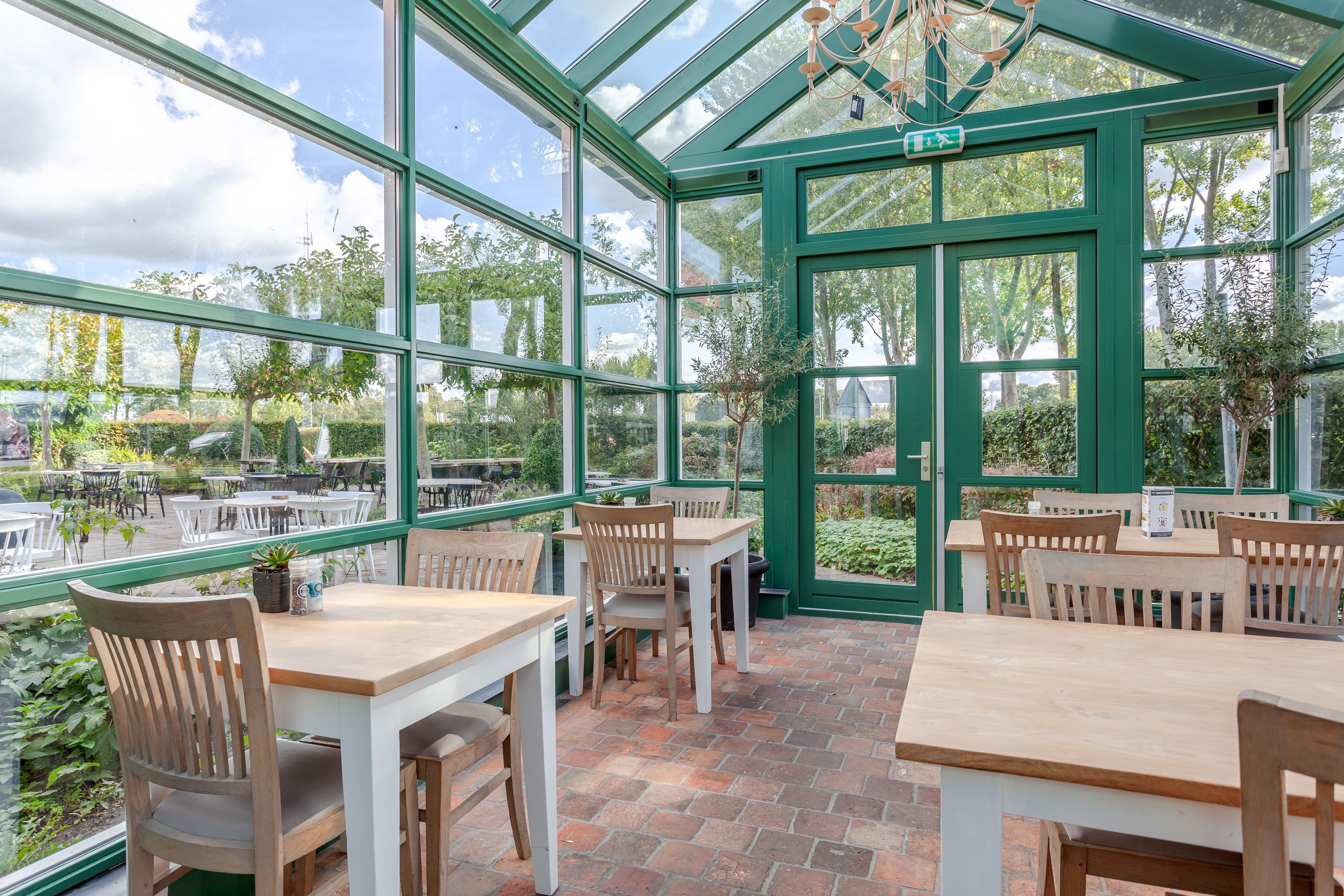A conservatory with tables and chairs, large windows, and a brick floor.