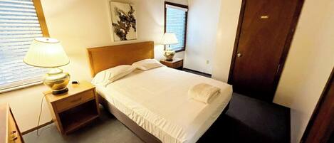 Una camera da letto con un letto, comodini, una lampada, un quadro e una porta.
